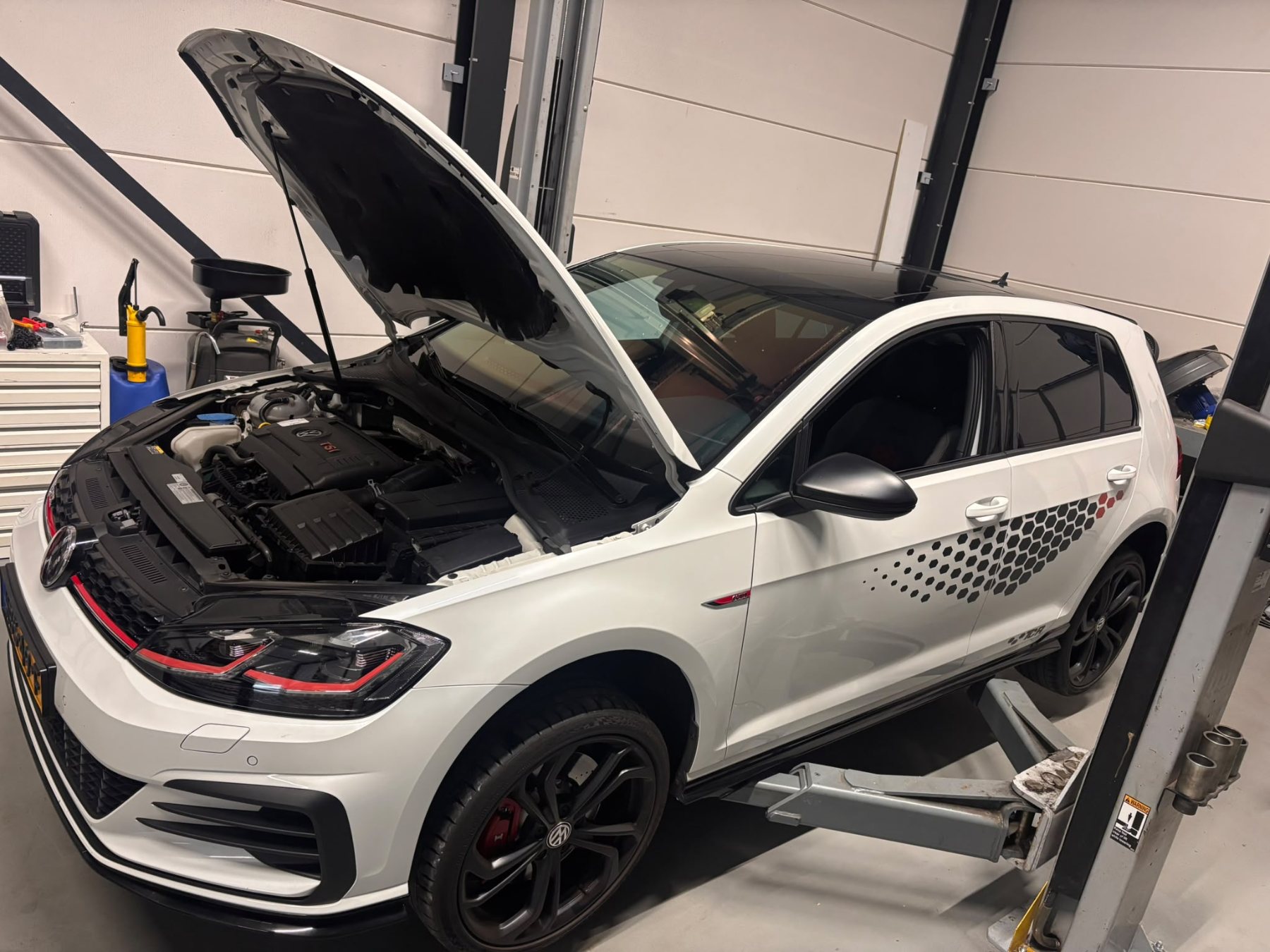 Volkswagen Golf GTI met open motorkap op de brug in de werkplaats van DOUWTECH